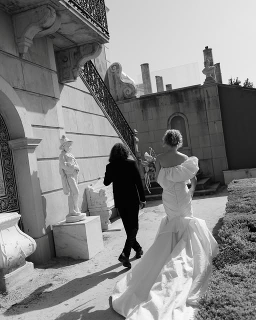 A bride and groom walking beside ornate stone architecture