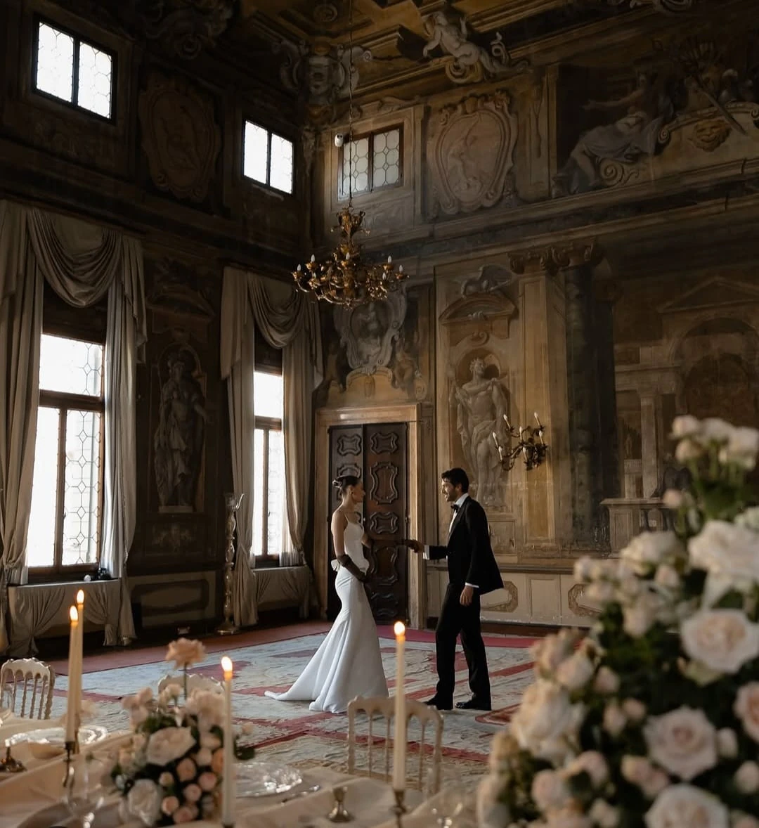 A bride and groom reaching towards each other inside an ornate Italian palazzo