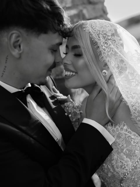 A bride and groom smiling closely beneath a lace veil