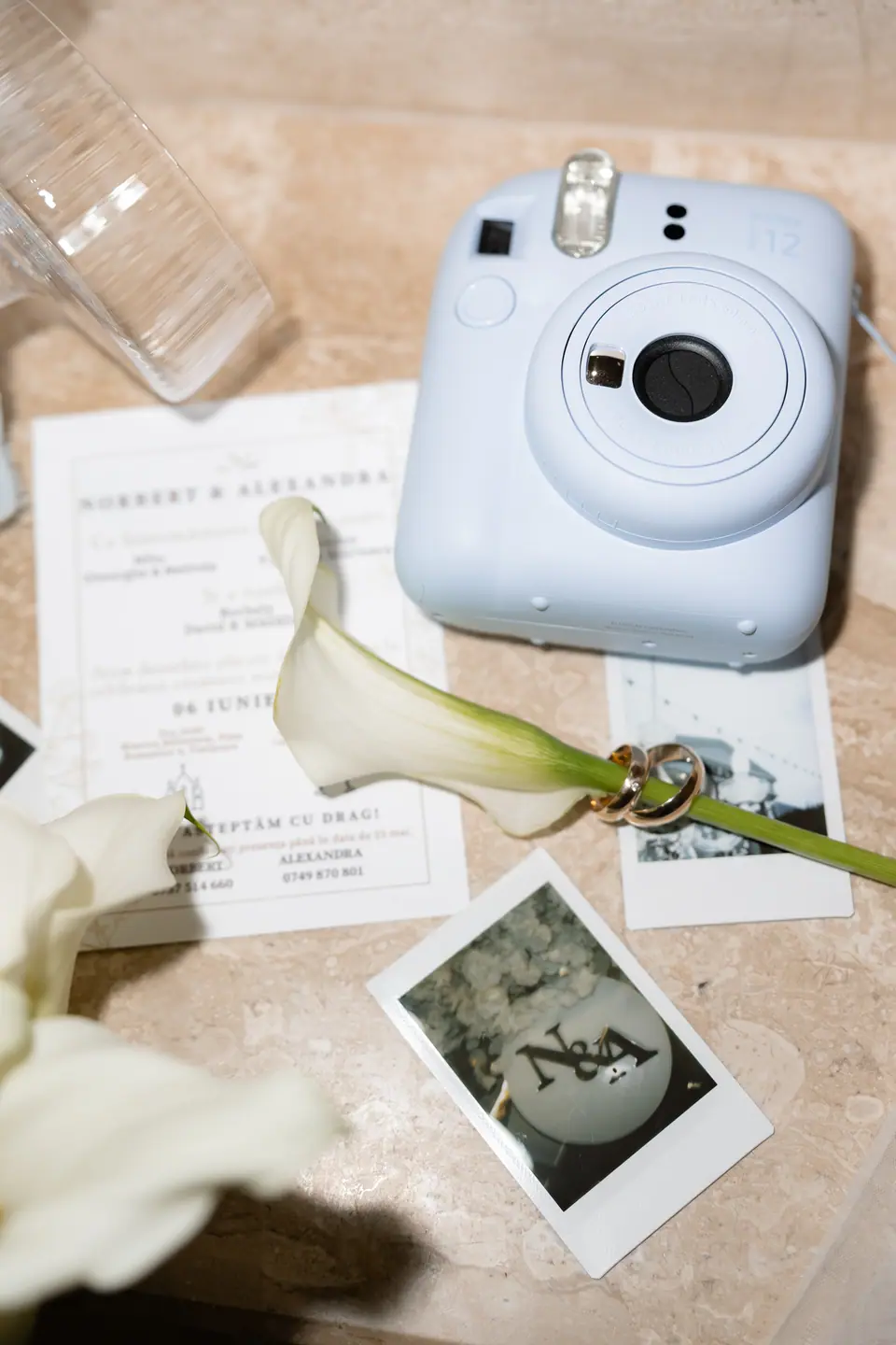 A pale blue instant camera, invitations and a Polaroid of the couple laid out with calla lilies