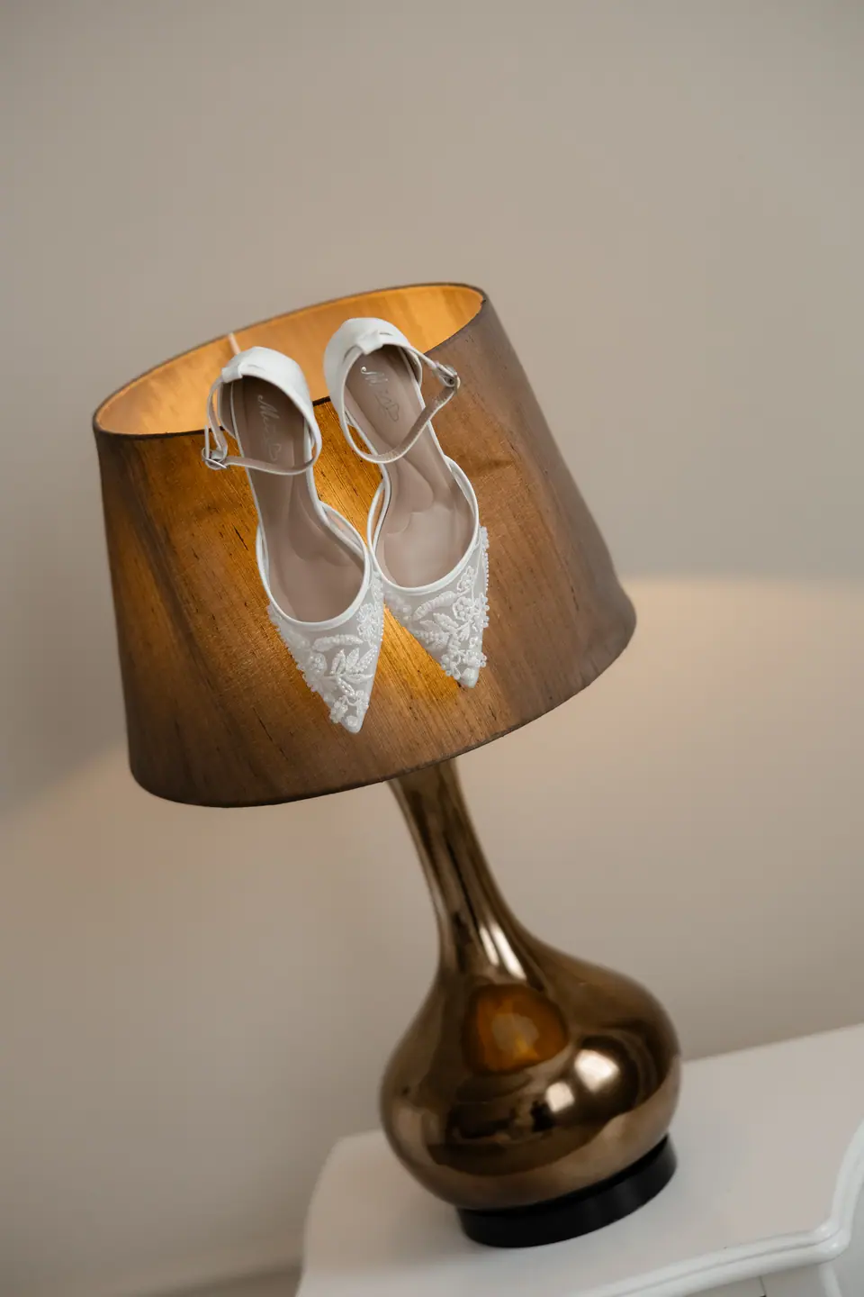 White beaded bridal shoes resting on a bronze lamp shade