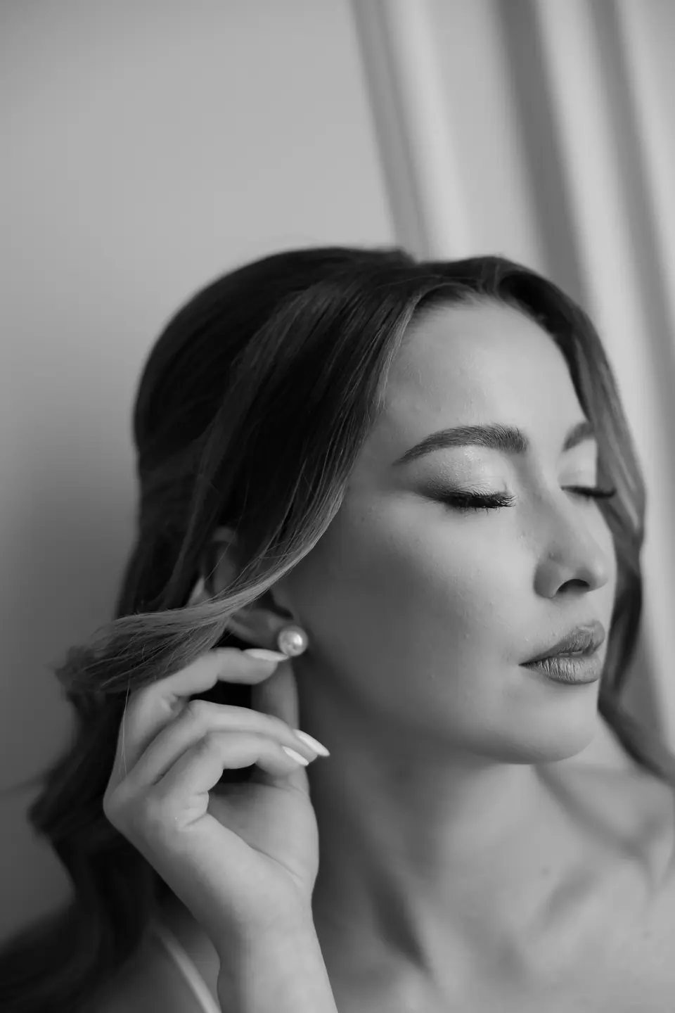 Black and white close portrait of Alexandra with her eyes closed, touching her pearl earring