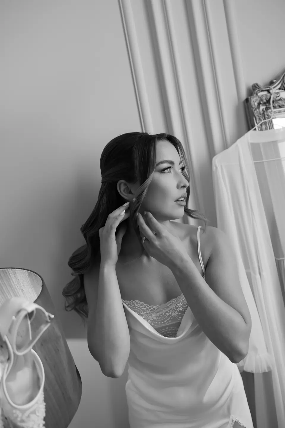 Alexandra in black and white adjusting her earring, shoes on the lamp beside her