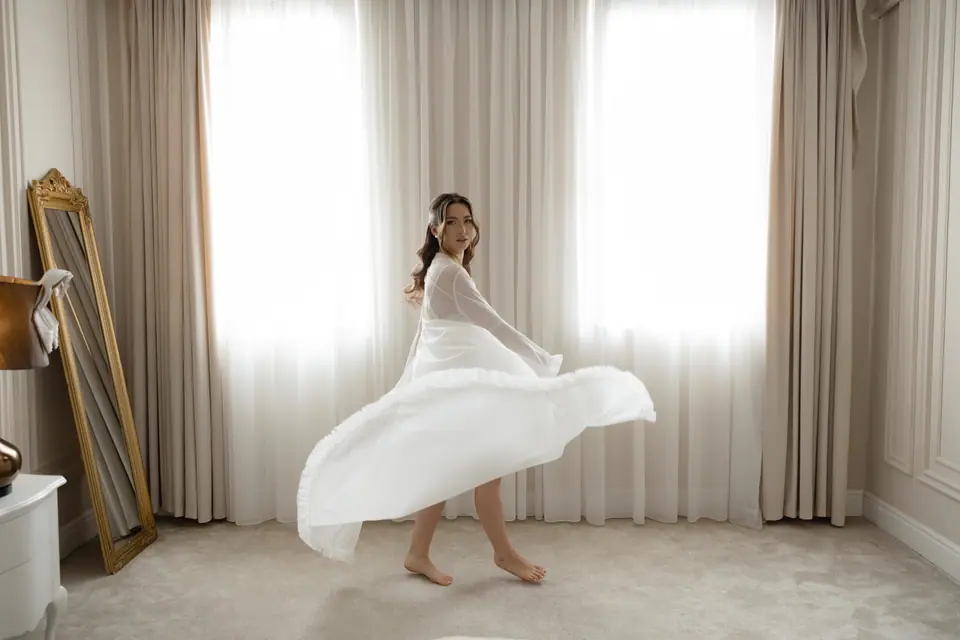 Alexandra spinning in her white robe in front of tall curtains