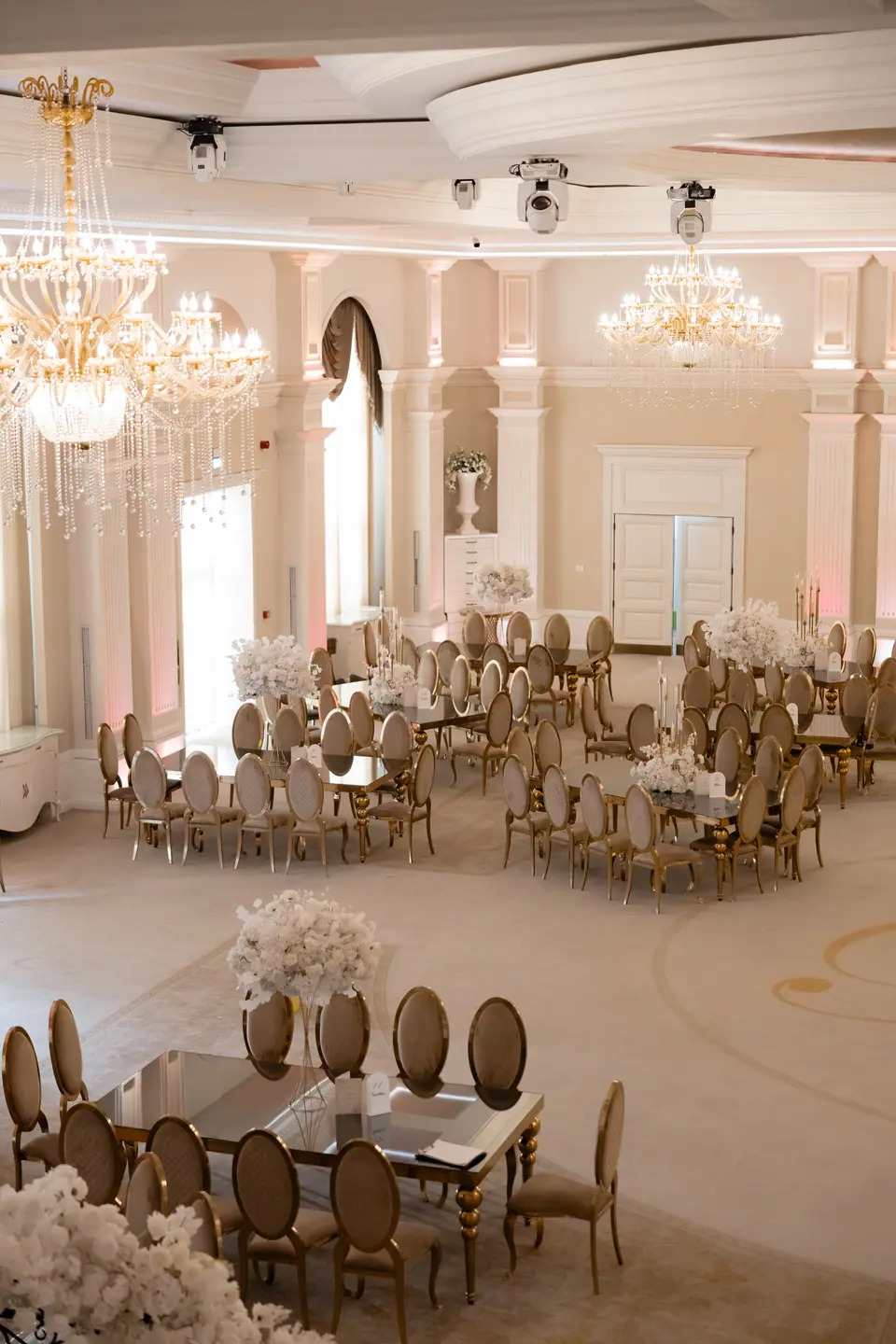 Reception hall seen from above, set with long tables, gold chairs and white flowers