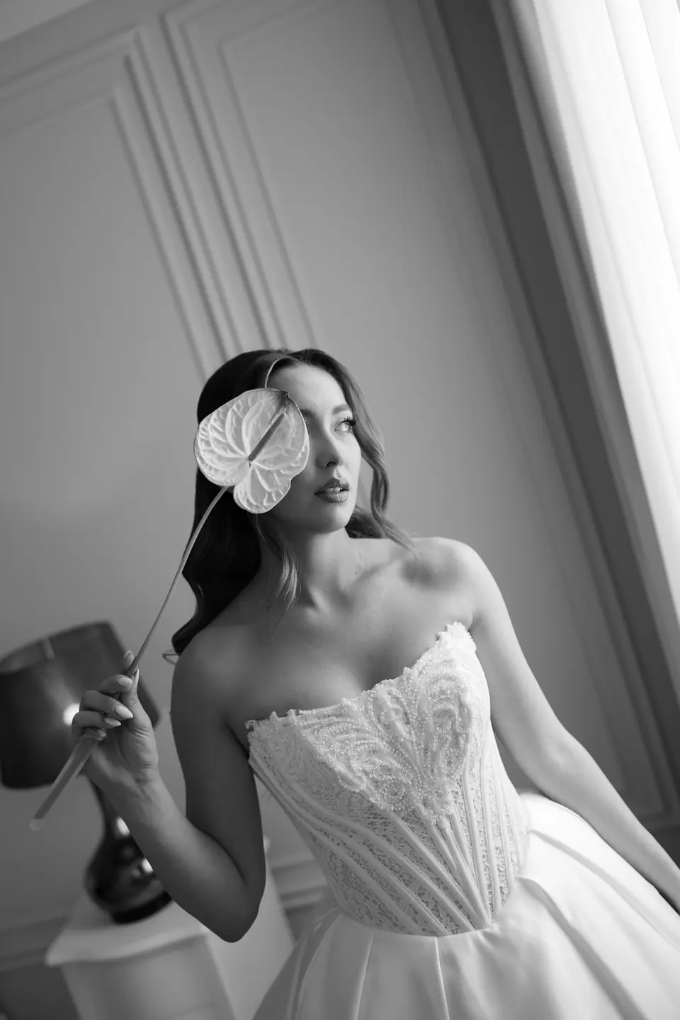 Black and white portrait of Alexandra holding a white anthurium flower in front of her eye