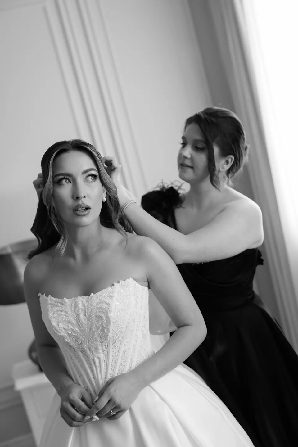 A friend pinning Alexandra’s hair as she fastens her bodice, in black and white
