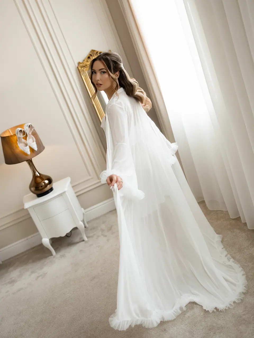 Alexandra in her white robe and veil looking over her shoulder by a gold mirror
