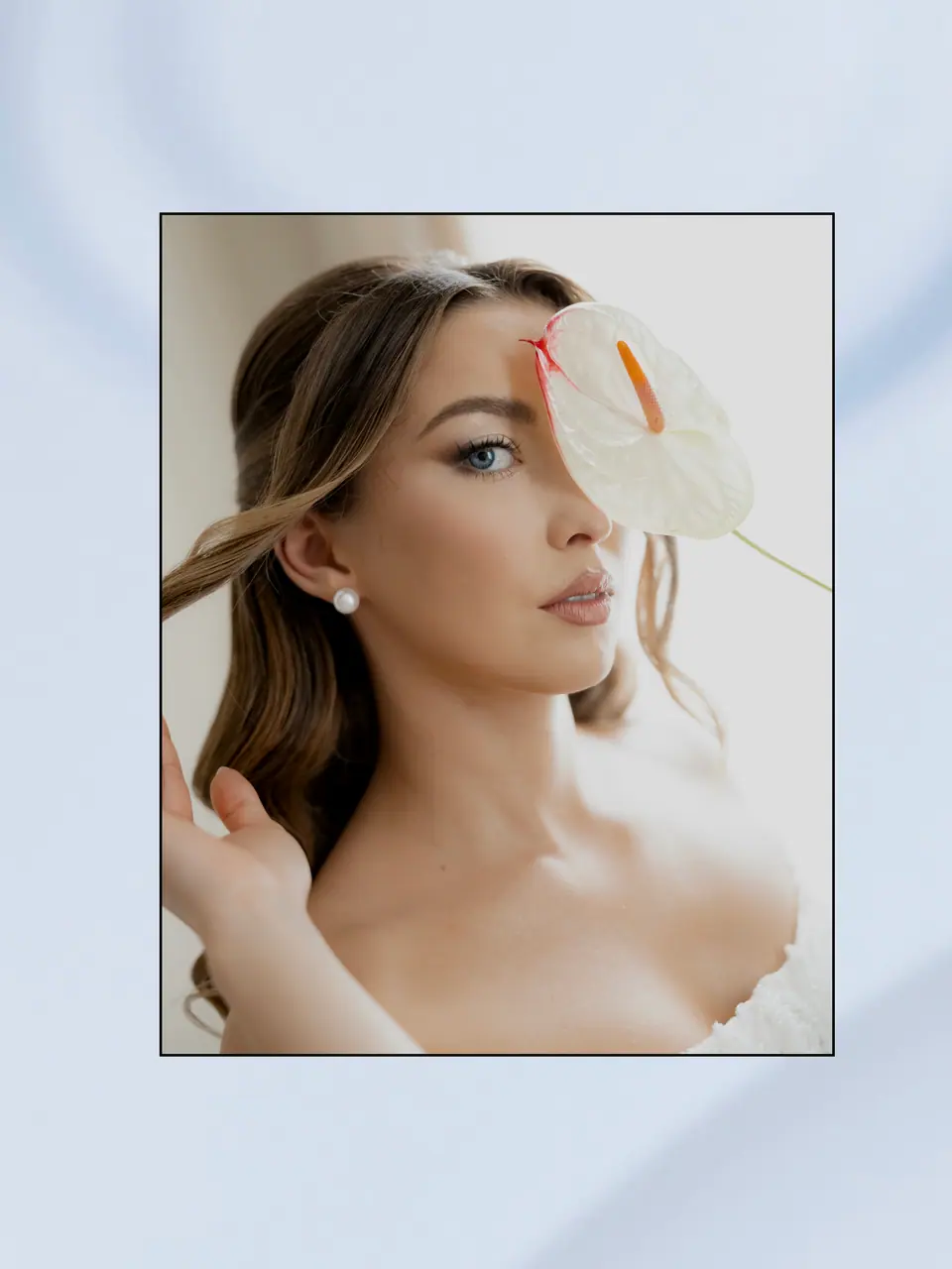 Alexandra with a white anthurium flower in front of her eye on a pale blue background