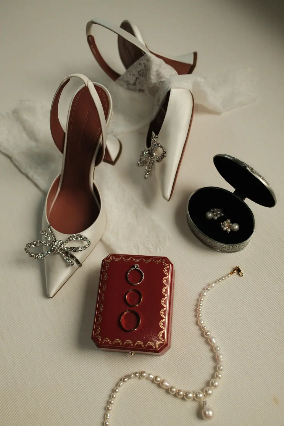 Bridal shoes, a ring box and a pearl necklace laid out on a white surface
