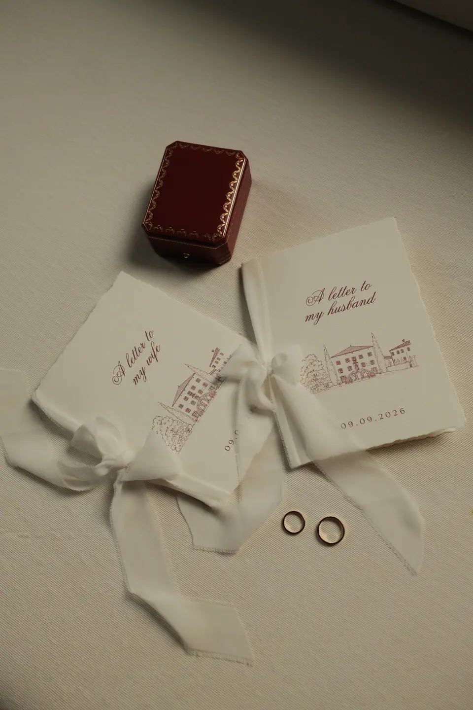 Letters to “my wife” and “my husband” tied with ribbon, a red ring box and two gold bands