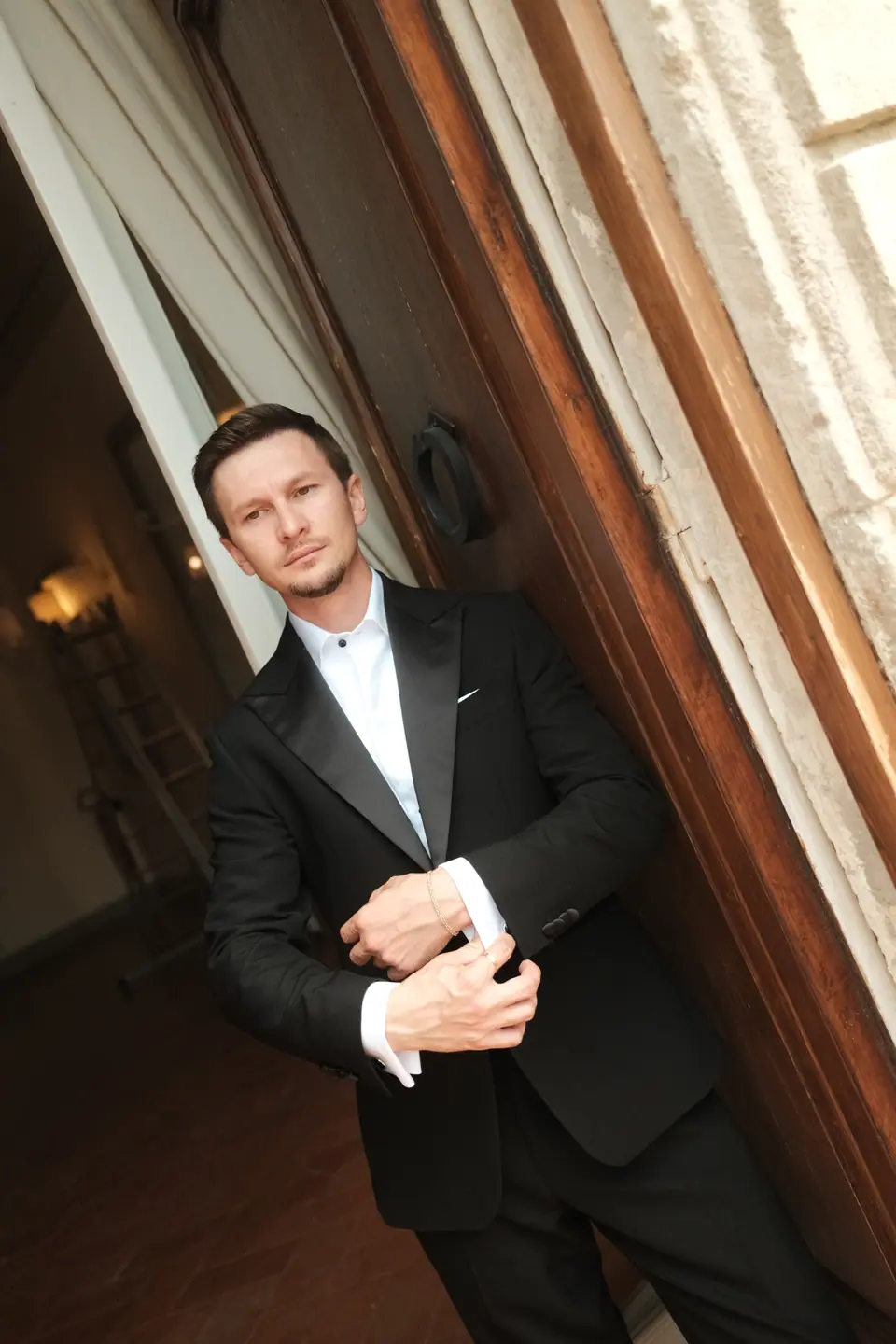 Silviu fastening his cufflinks against a wooden shutter