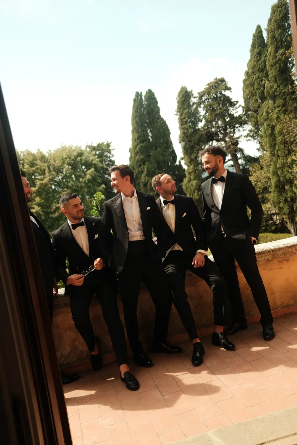 Silviu and his groomsmen in tuxedos on a stone balcony among the cypresses