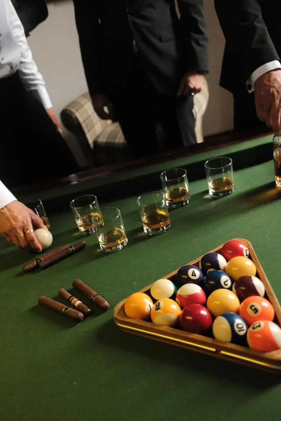 Whiskey glasses, cigars and racked balls on a green billiard table