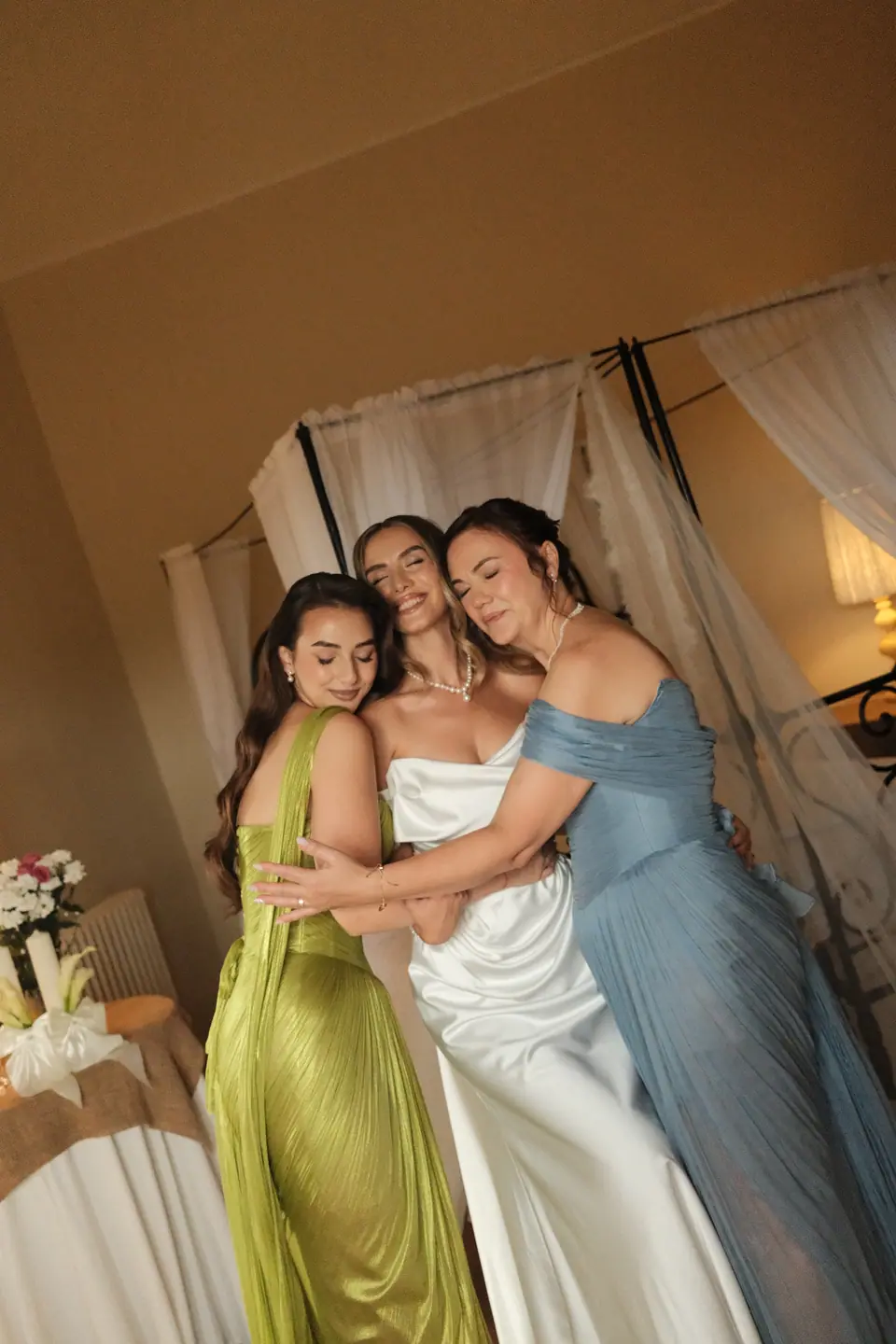 Ana hugging two bridesmaids in green and blue gowns