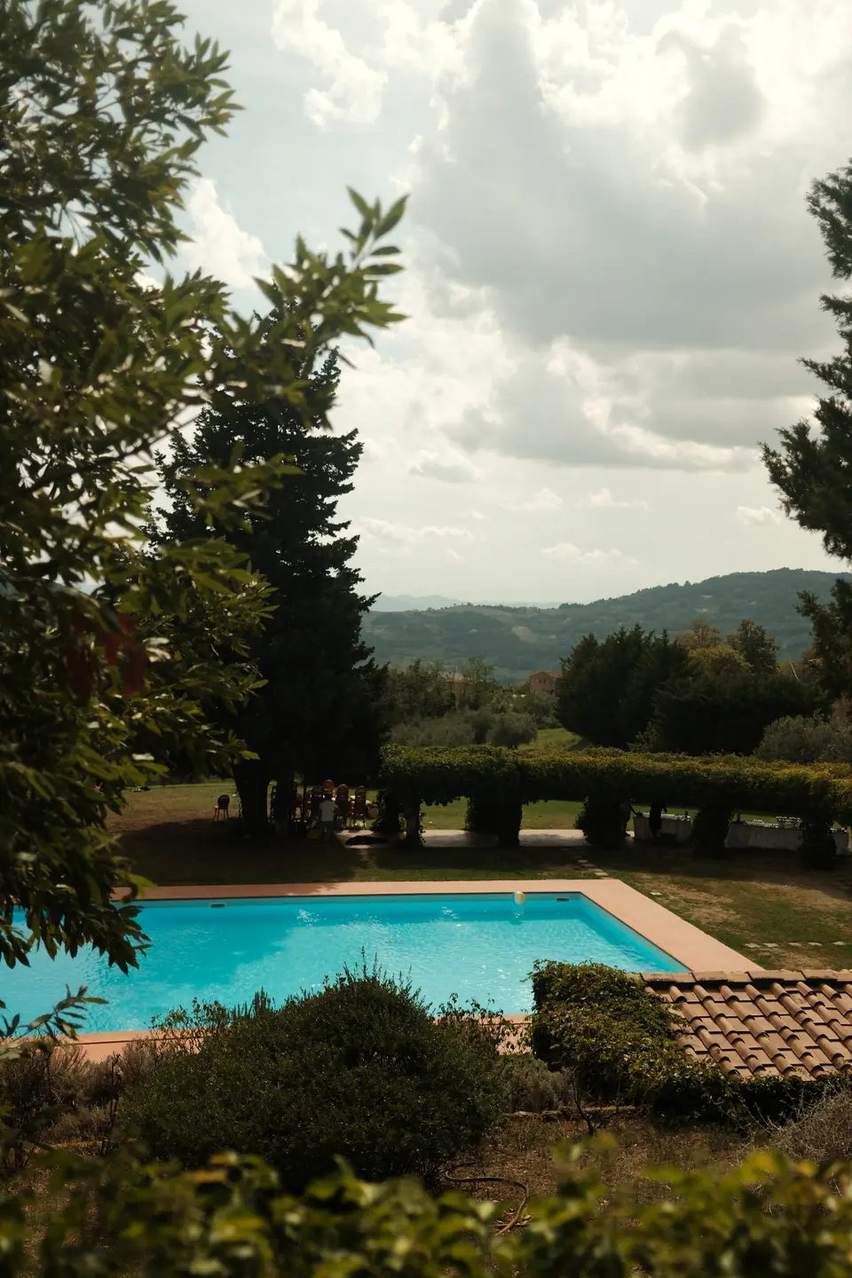 The villa pool below the garden, the Tuscan hills beyond the trees