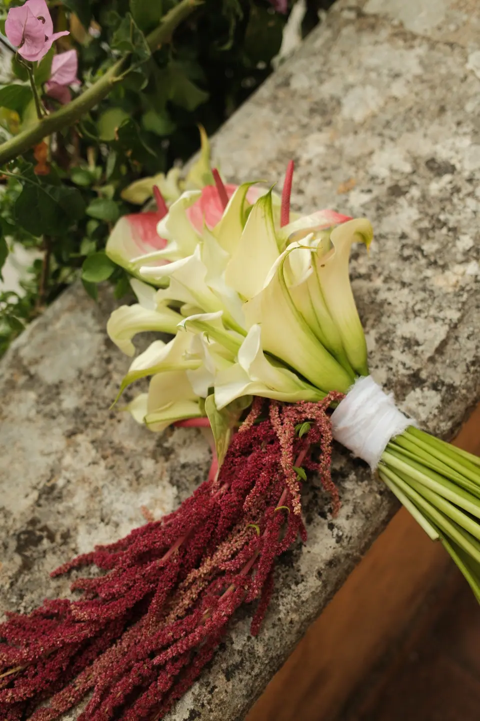 Ana’s bouquet of calla lilies and red amaranthus resting on a stone wall
