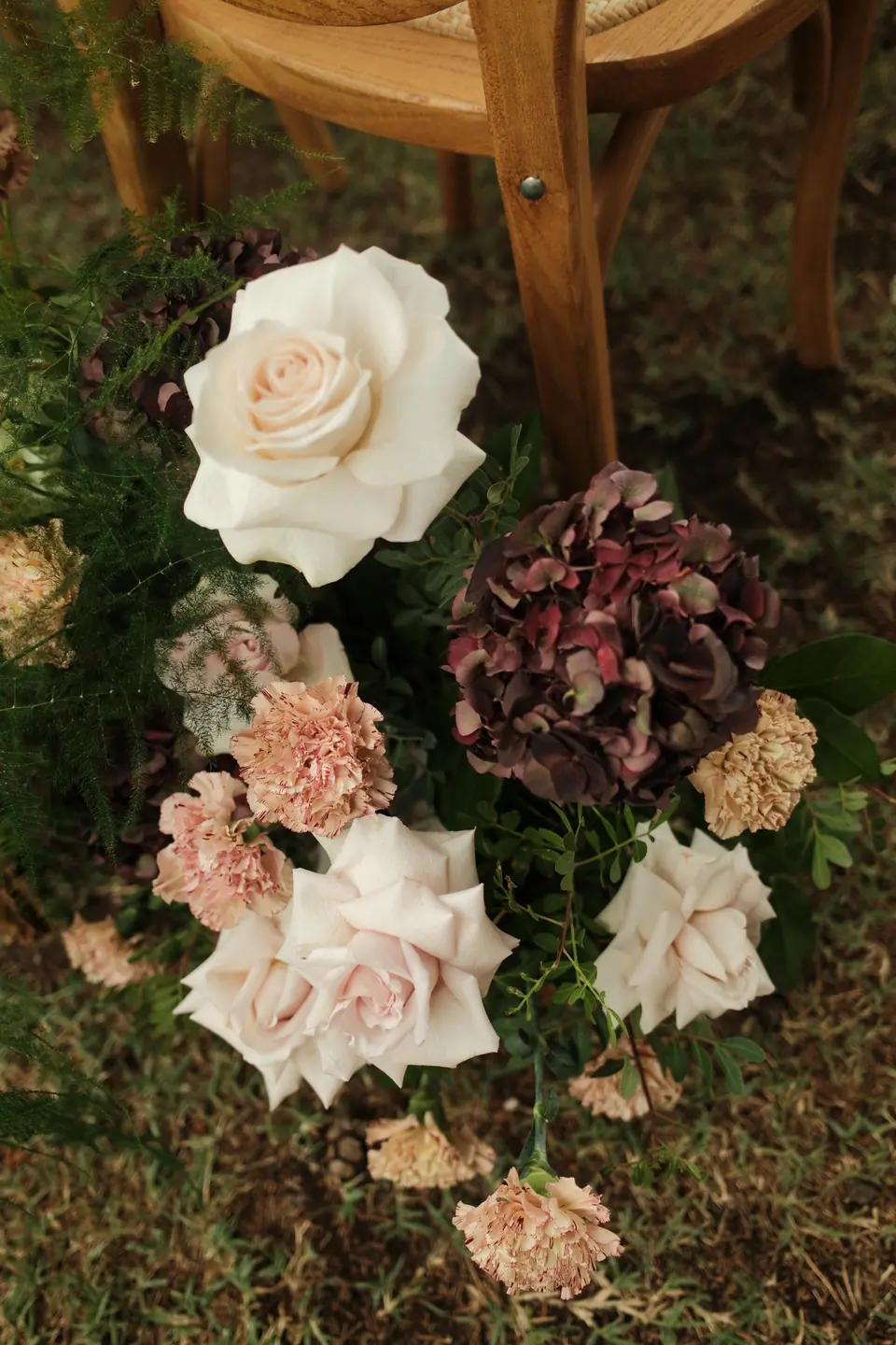 Roses, carnations and dark hydrangea arranged at the foot of a ceremony chair