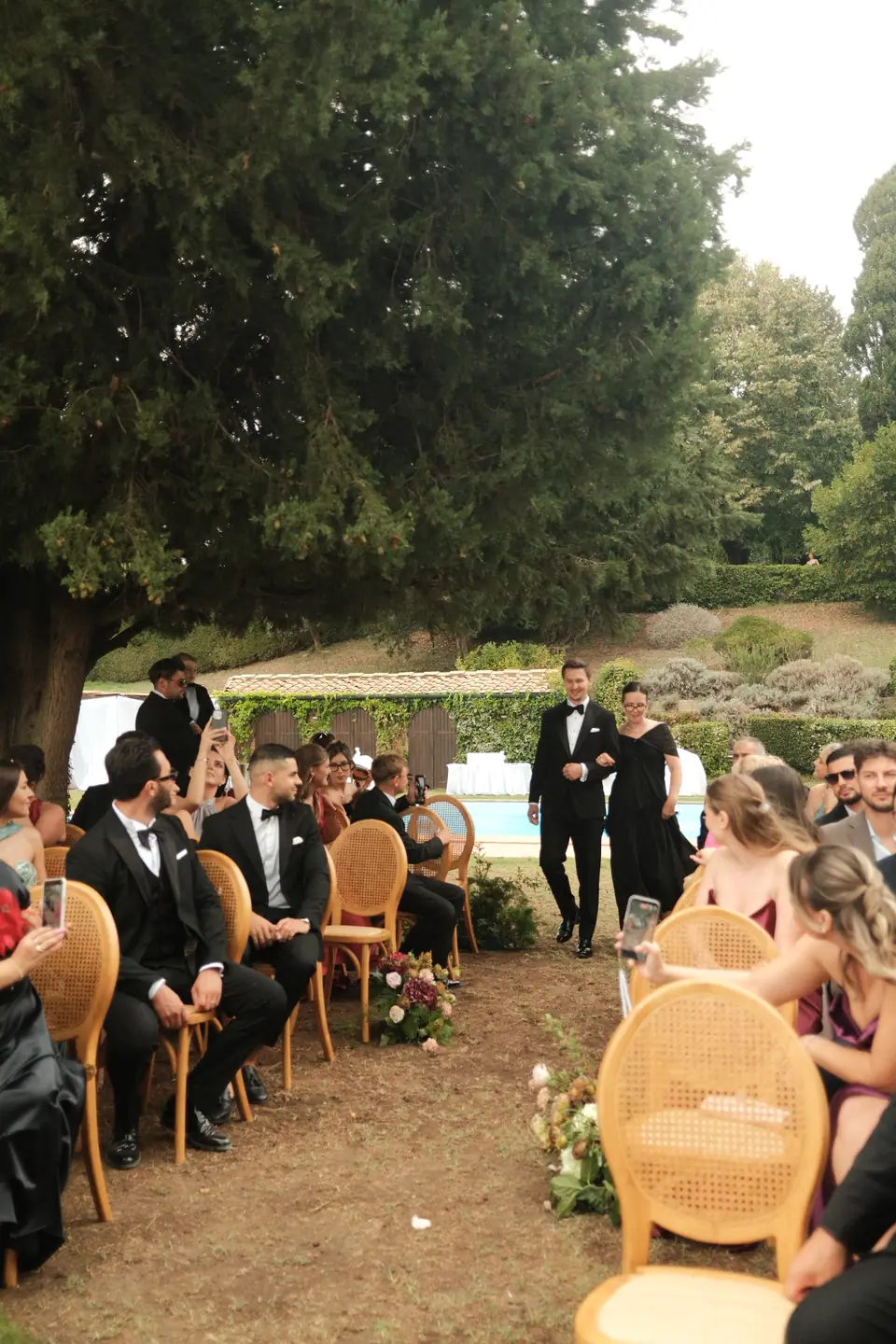 Guests seated in rattan chairs under the trees as the ceremony begins