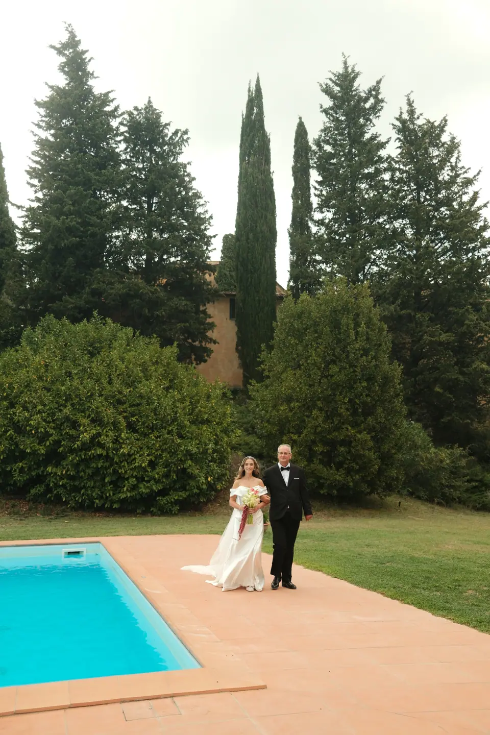 Ana walking past the pool towards the ceremony on a man’s arm