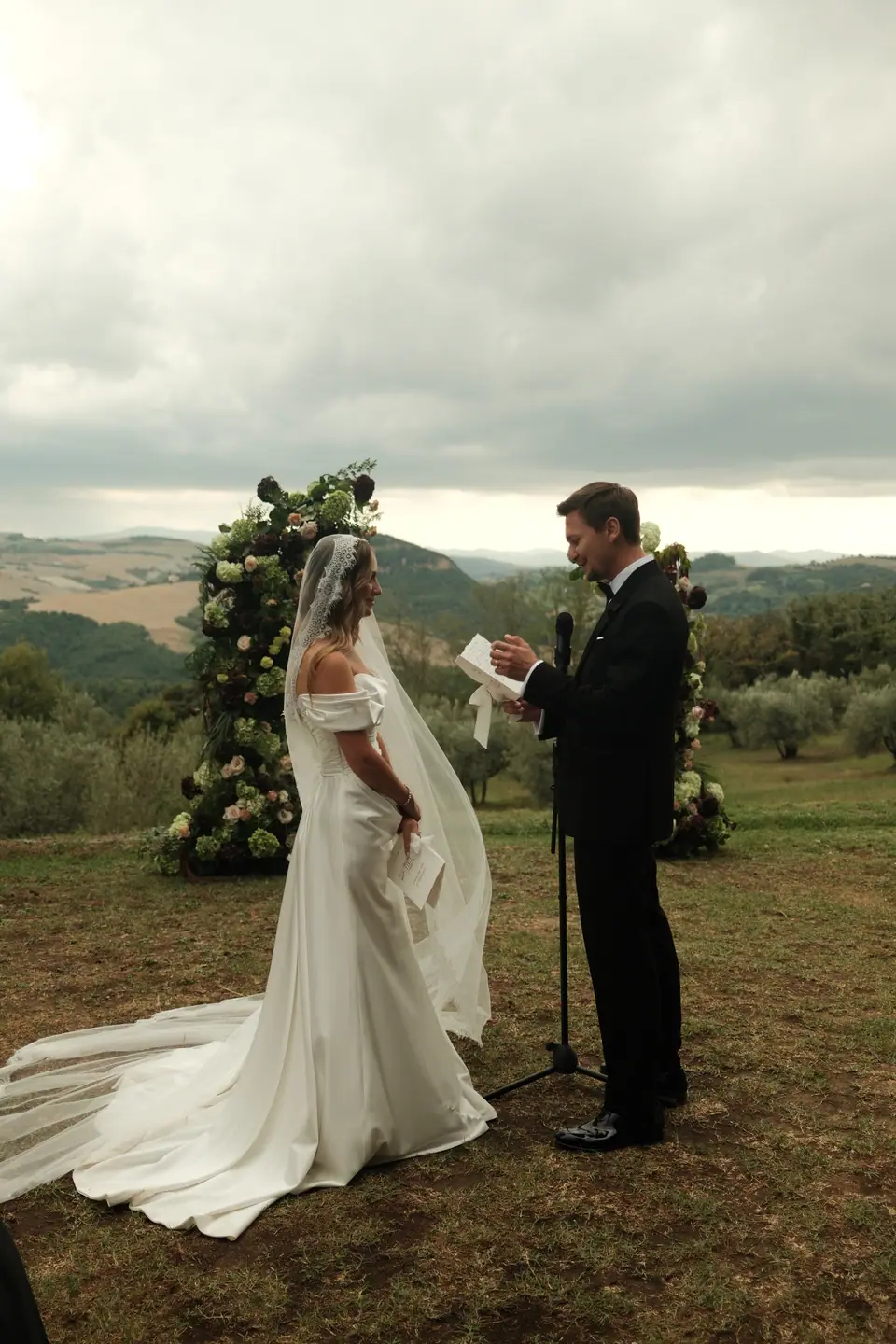 Silviu reading his vows to Ana between the floral pillars above the hills