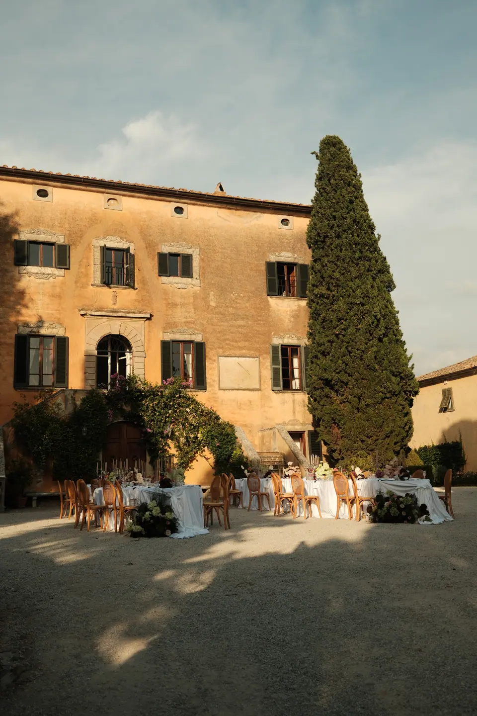 Dinner tables set in the villa courtyard beside a tall cypress
