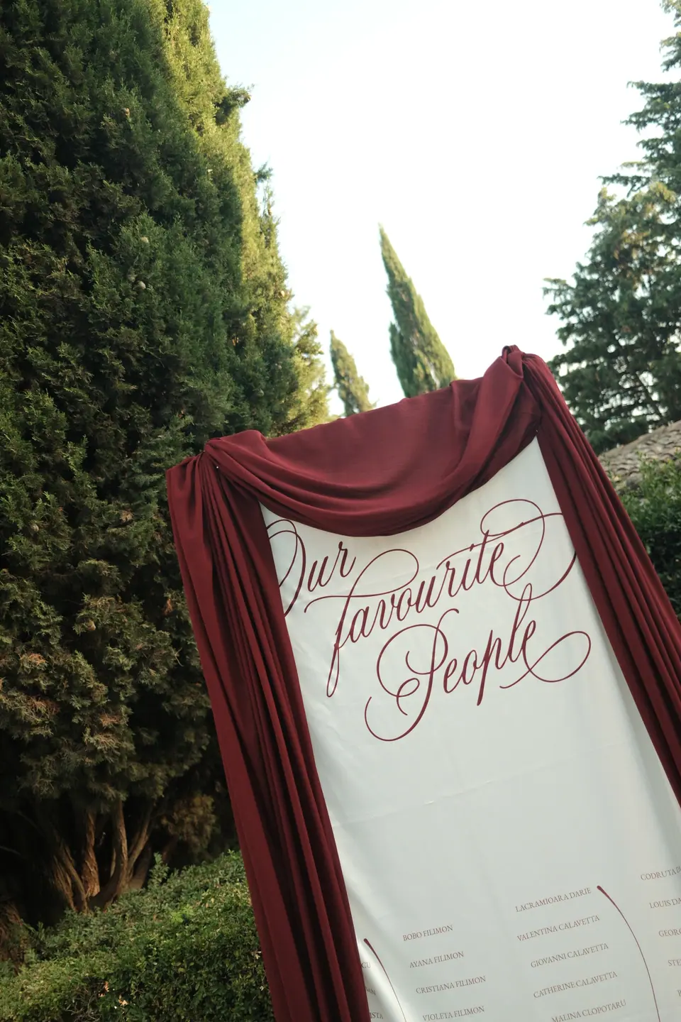 The burgundy-draped seating chart set against tall cypresses