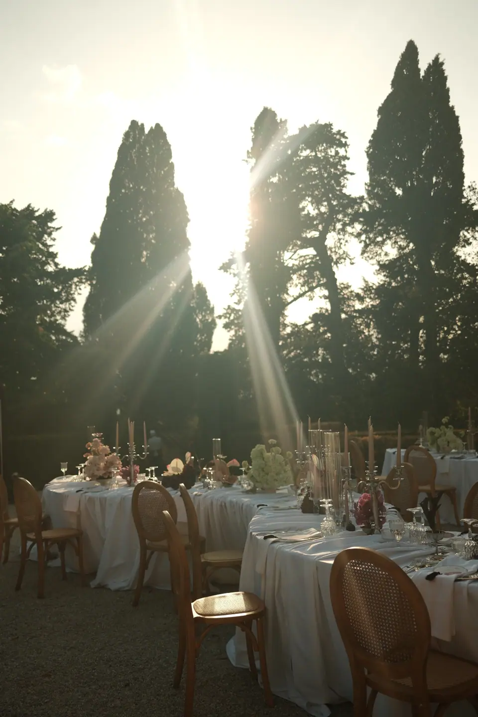 Evening sun through the cypresses across the empty dinner tables