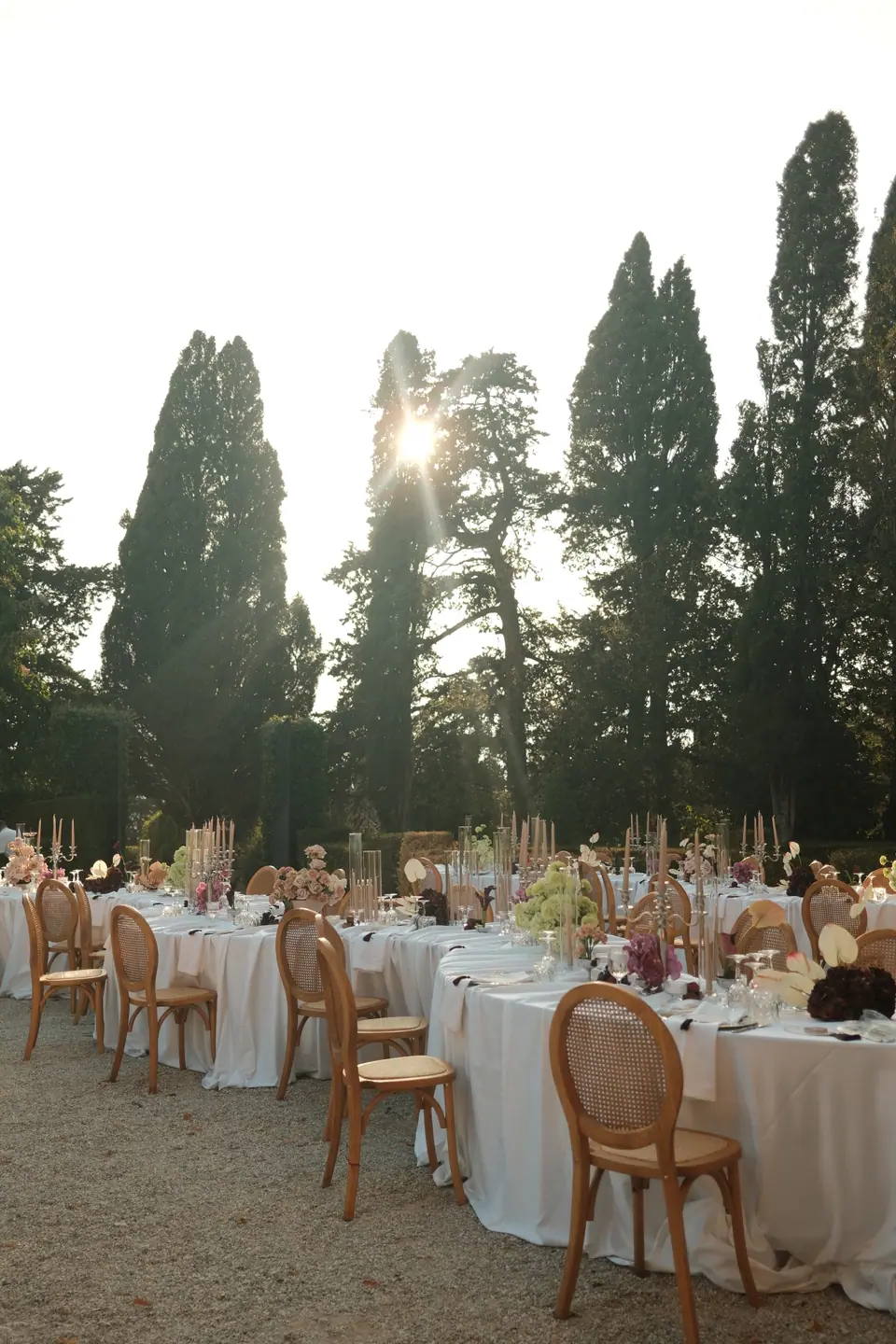 Rattan chairs around white tables as the sun sets behind the cypresses