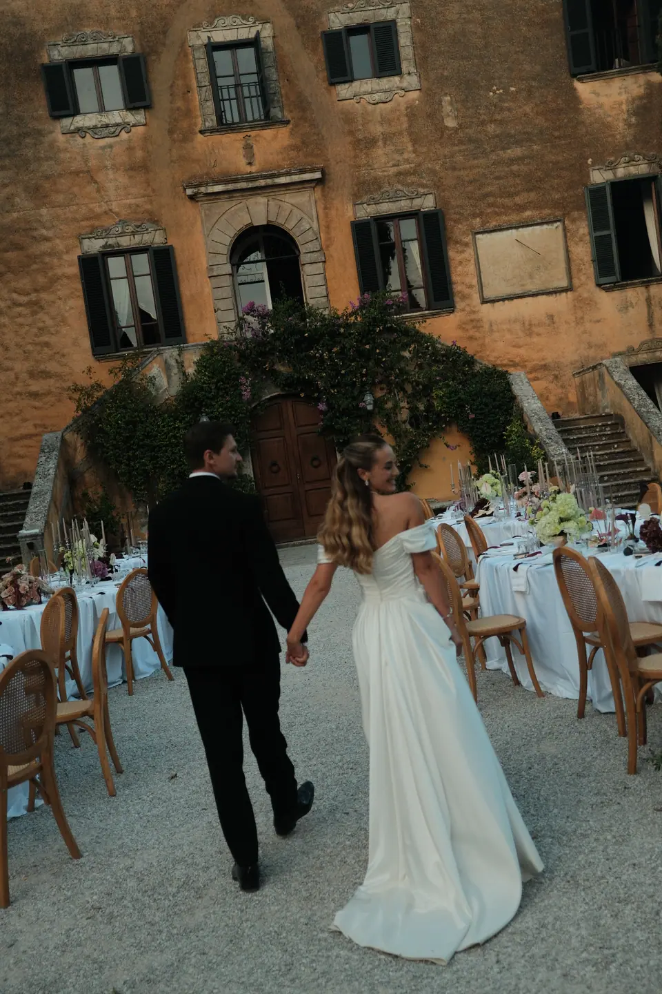 Ana and Silviu walking hand in hand past the dinner tables in front of the villa