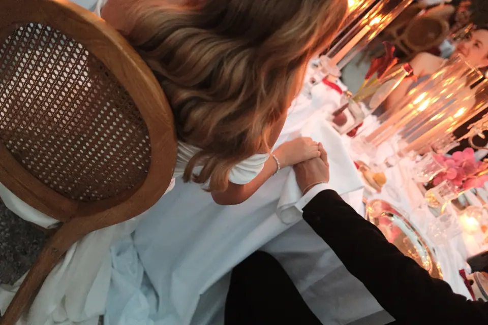 Ana and Silviu holding hands at the table, seen over a rattan chair