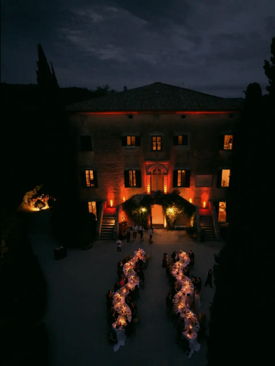 Aerial view of the villa lit up at night, two candlelit tables in the courtyard