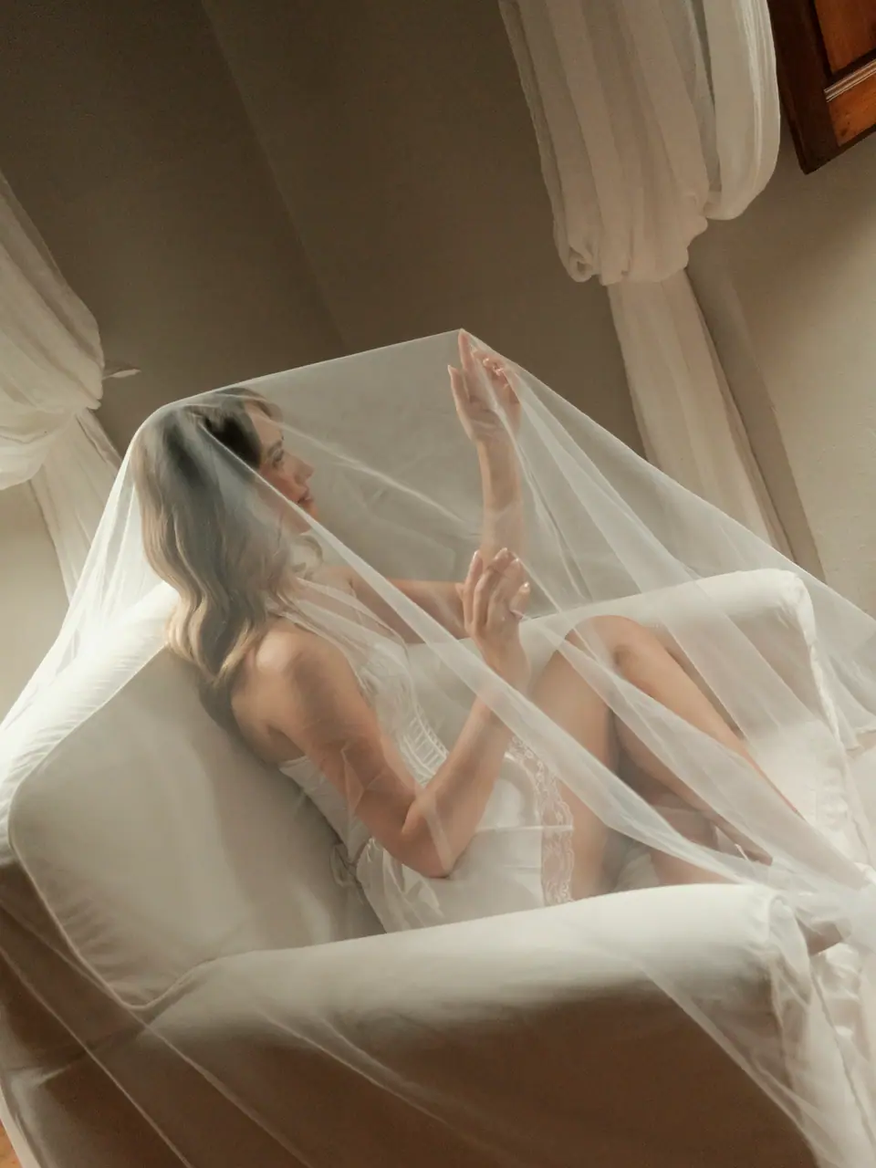 Ana reaching up through her veil on the white armchair