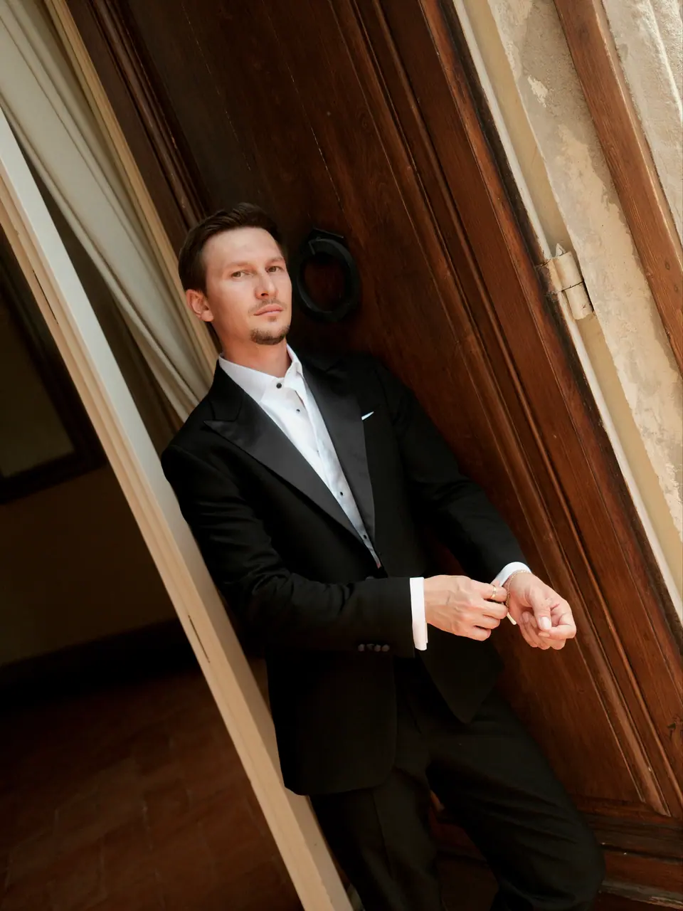 Silviu leaning in a wooden doorway, fixing his cuffs