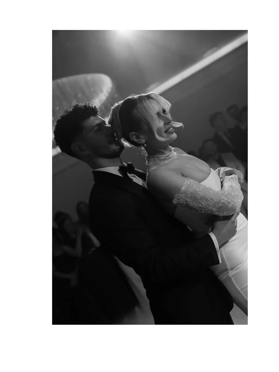 Black and white photograph of Bogdan holding Andreea from behind under the reception lights, framed in white