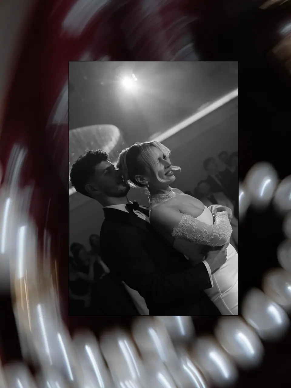 Black and white photograph of the couple at the reception, set inside a blurred frame of pearls and deep red