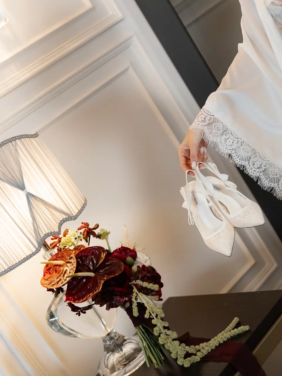 Andreea holding her shoes beside a red bouquet and a lamp