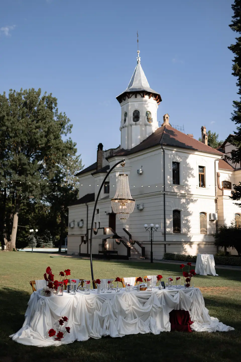 A white manor with a turret above the lawn, the head table draped in white with red roses
