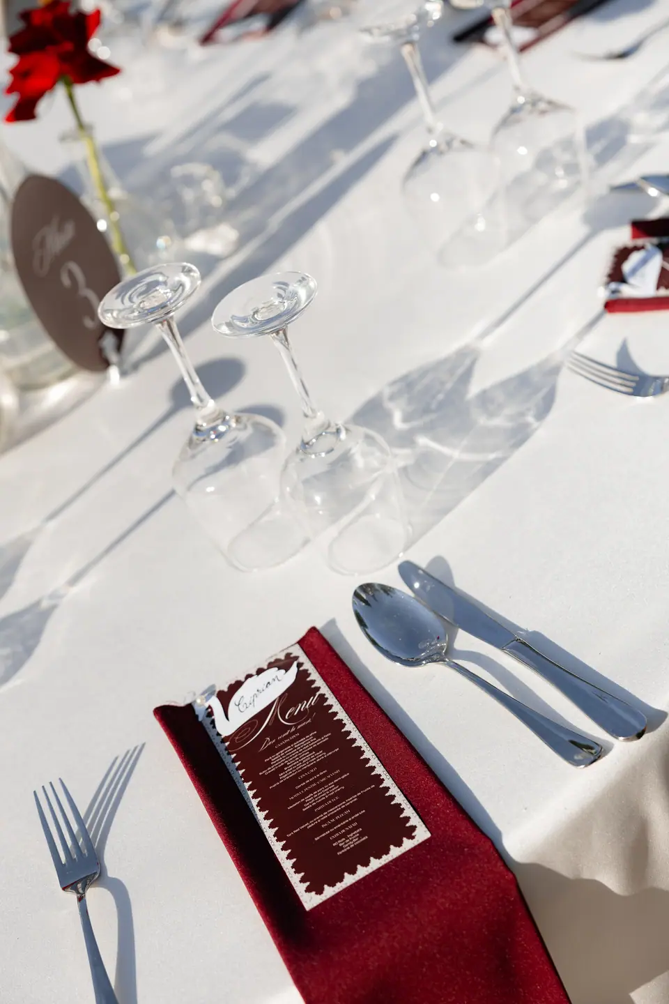 A place setting with a burgundy napkin, the menu and wine glasses in sunlight