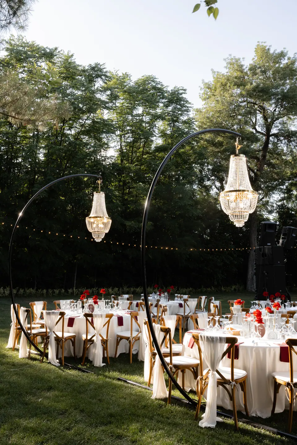 Crystal chandeliers on curved stands above dinner tables set on a lawn