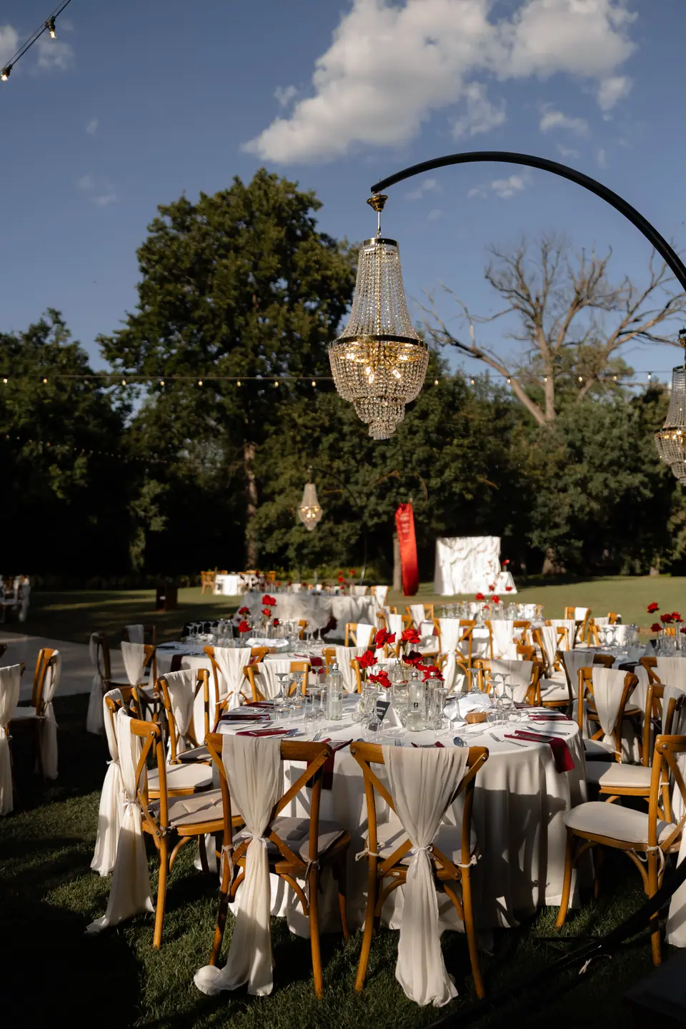 Crystal chandeliers hanging above round dinner tables in a garden