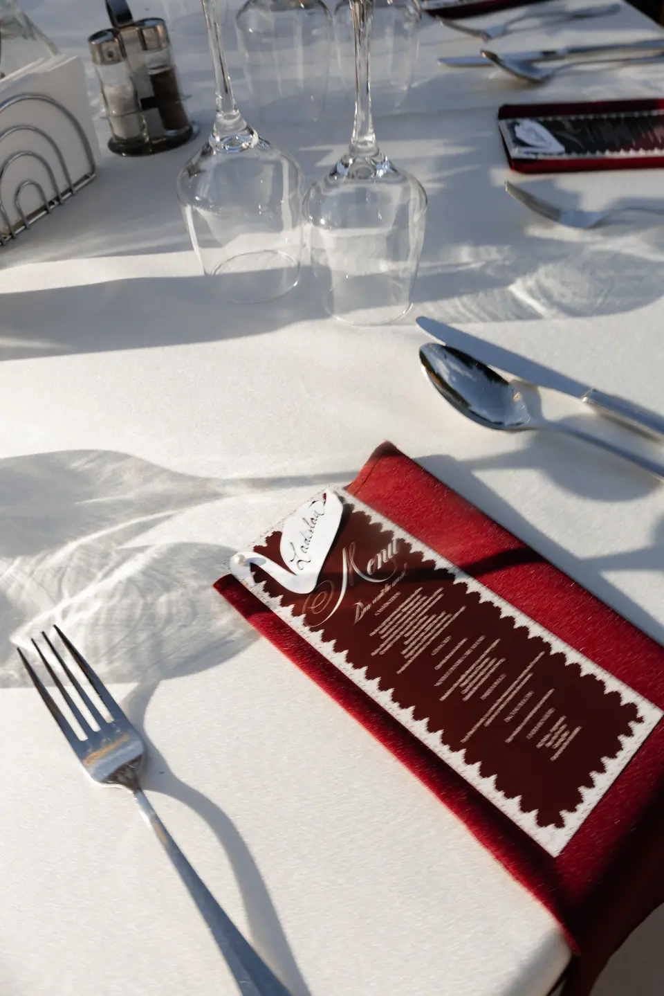 A burgundy napkin with a deckle-edged menu card in sunlight