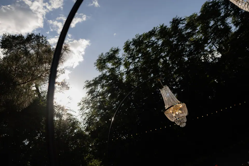 A chandelier hanging from an iron arch, string lights behind