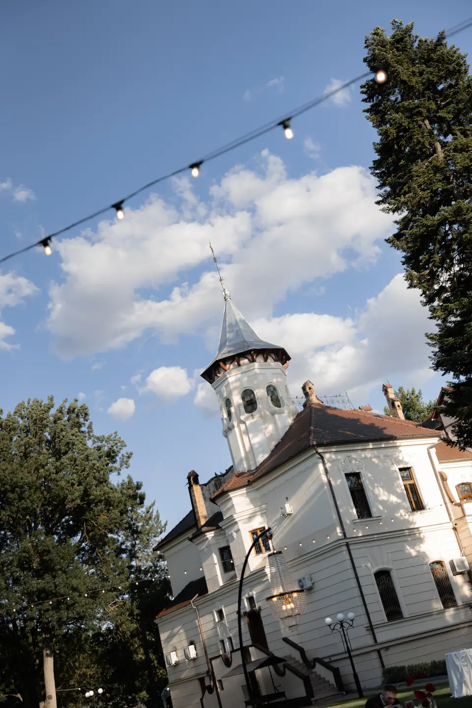 The white manor’s turret against the sky, string lights overhead
