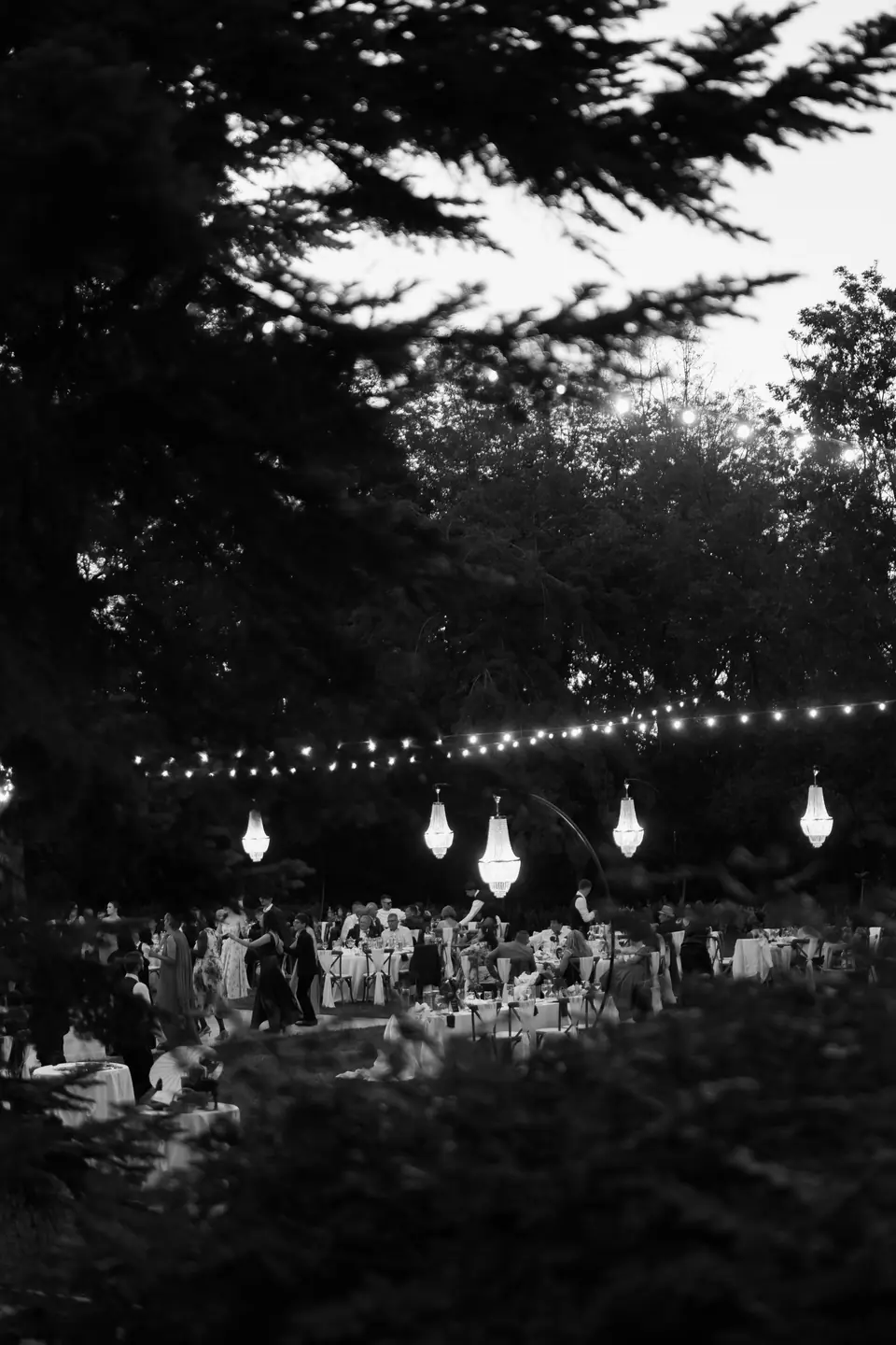 Black and white photograph of the reception beneath string lights and chandeliers