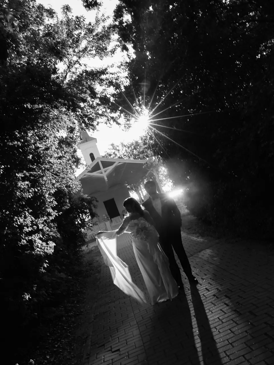 Black and white photograph of the couple walking along a brick path in the setting sun