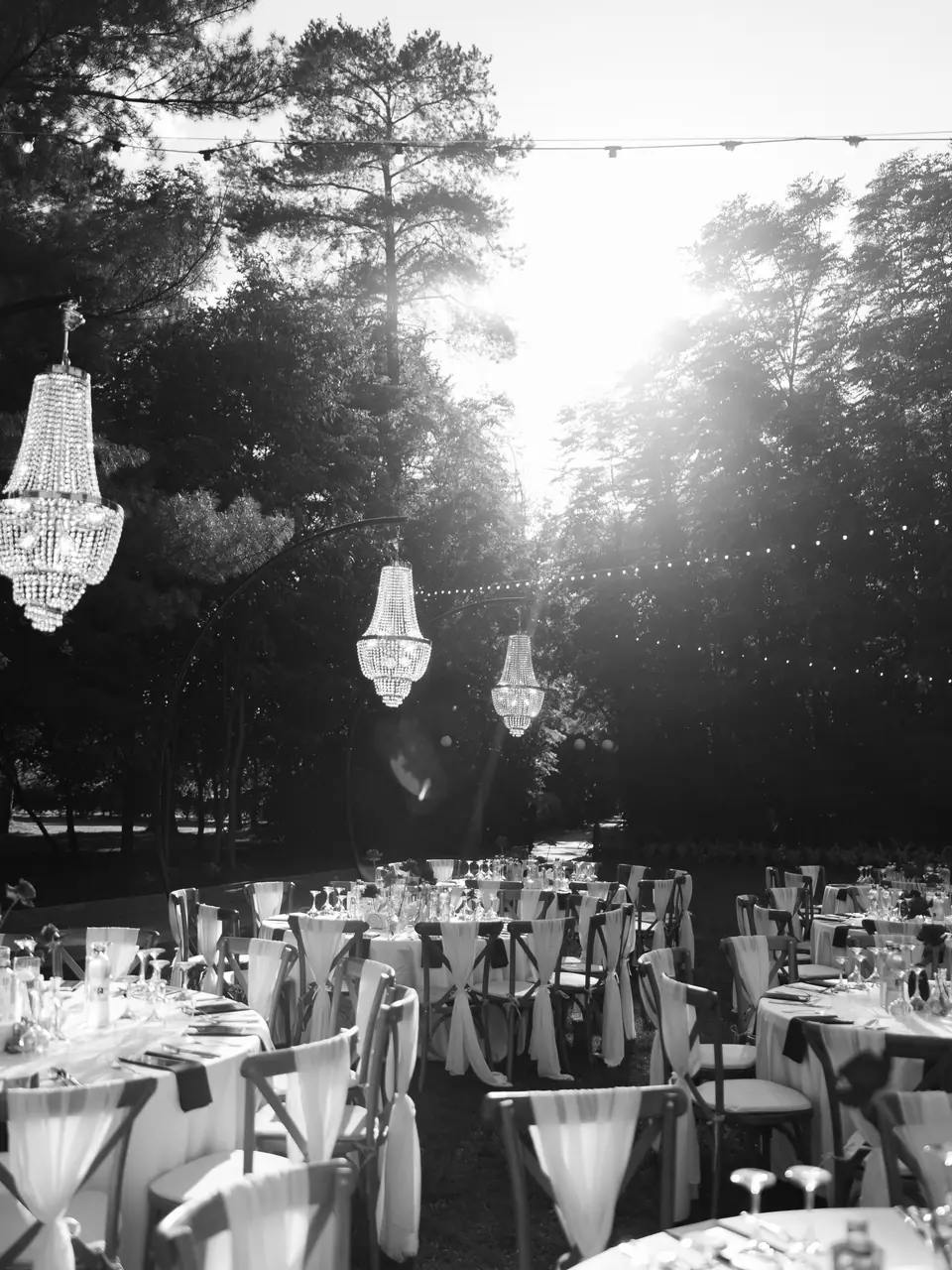 Black and white photograph of chandeliers hanging above the dinner tables in the trees