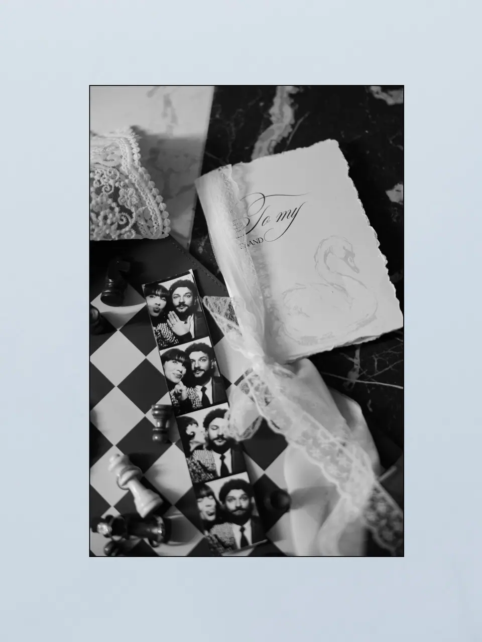 A note, lace and a photo-booth strip on a black and white chessboard, on pale blue
