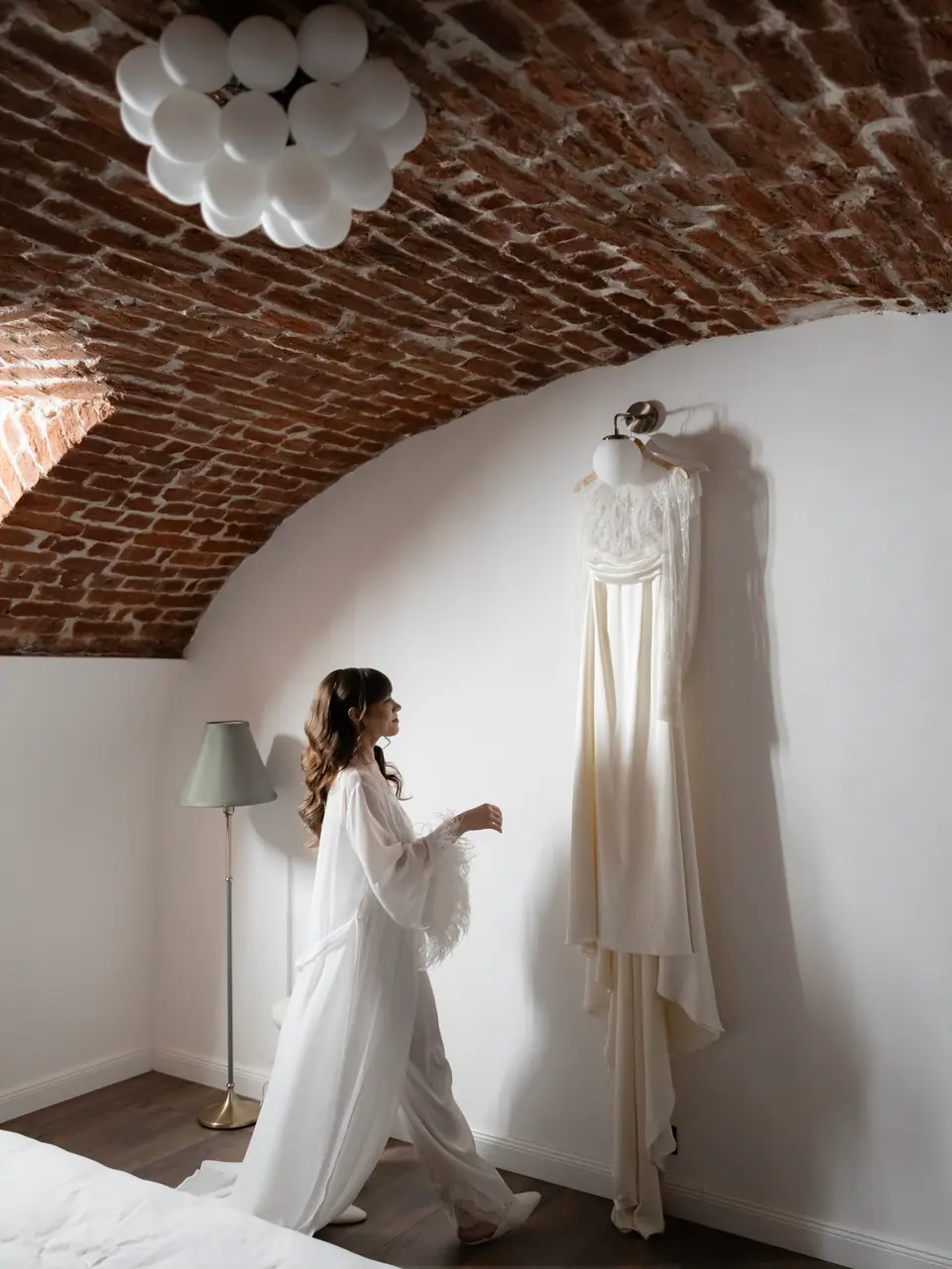 Bianca in her feathered robe looking up at her gown hanging on the wall