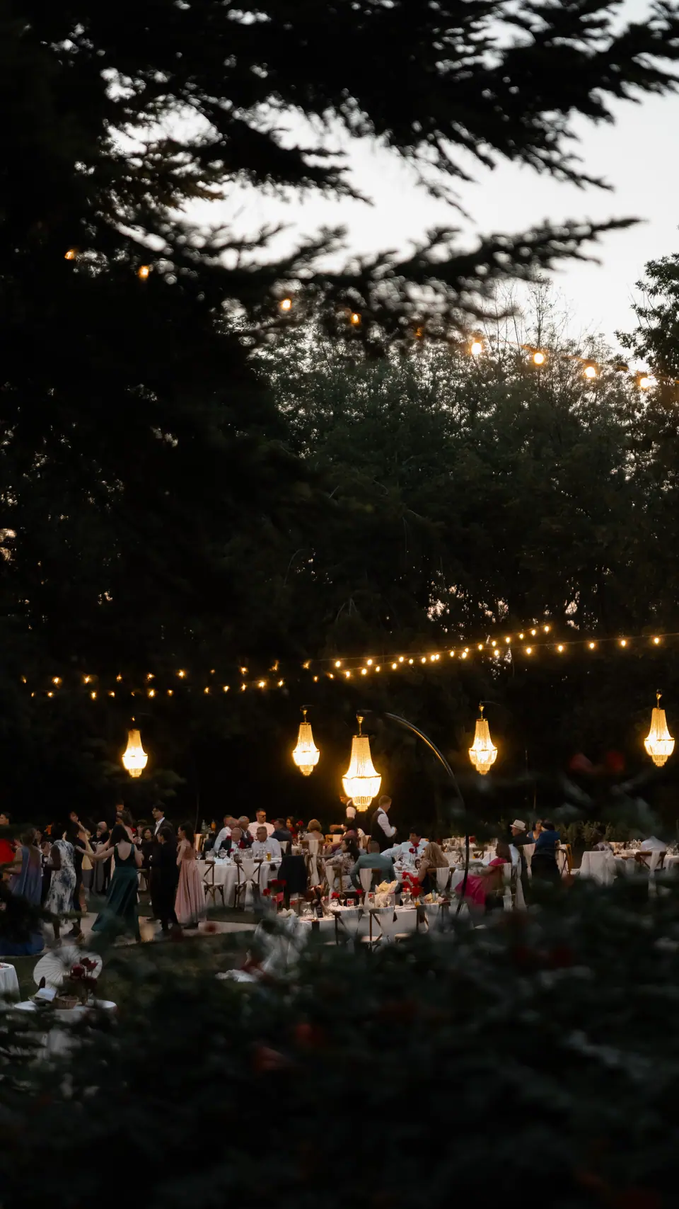 The reception glowing beneath string lights and chandeliers among the trees